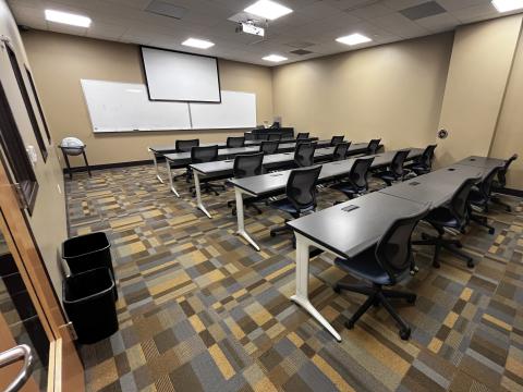 Photo of a room with five rows of desks and chairs and a screen at the front