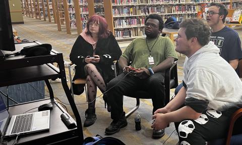 Four young adults with controllers staring at a TV screen.