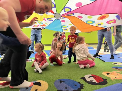 Toddlers playing under a colorful parachute