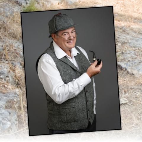 Man in gray vest and hat smiling while holding a pipe