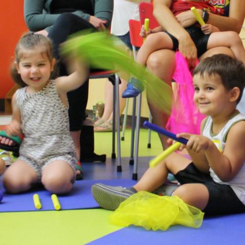 Children sitting on the floor waving colorful scarves as parents sit in chairs