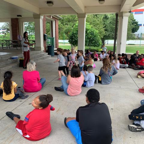 Kids sitting under a park pavilion watching a woman at the front