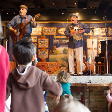 Two musicians on stage with children dancing below