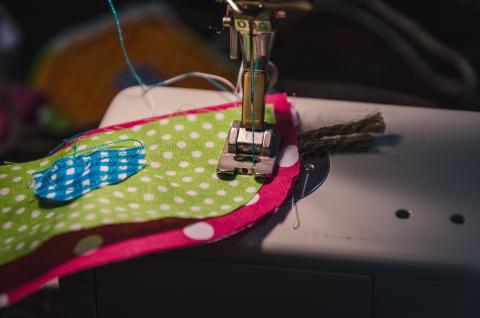 Close-up of sewing machine needle sewing together colorful layers of fabric