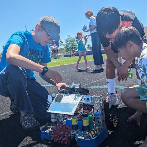 Teen working on a robot while younger kids watch