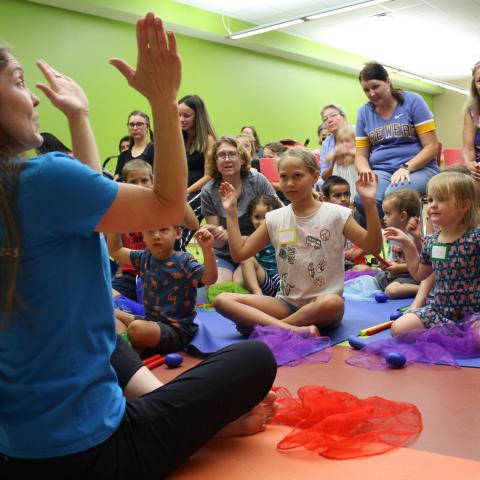 Children sitting on the floor clapping with an instructor at the front