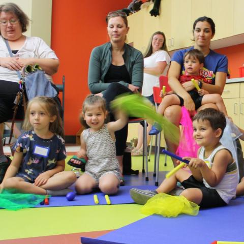 Children sitting on the floor waving colorful scarves as parents sit in chairs