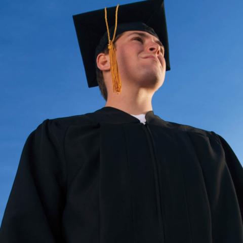 Young man in graduation gown and hat looking up into the sun