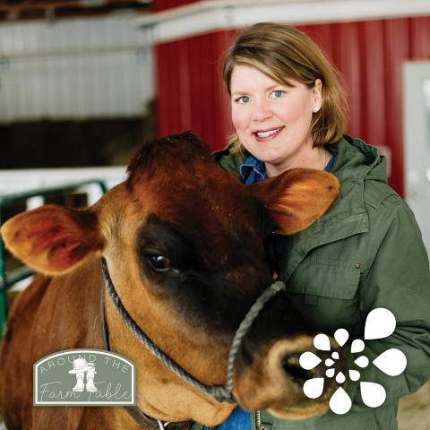 A woman standing next to a brown cow and holding it by its harness around its head.