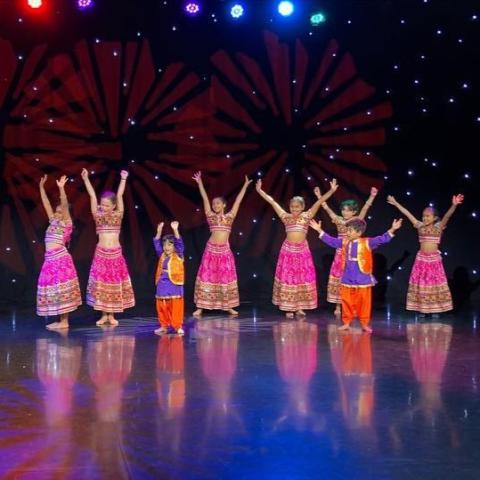 Children dressed in traditional Indian costumes dancing with their hands in the air