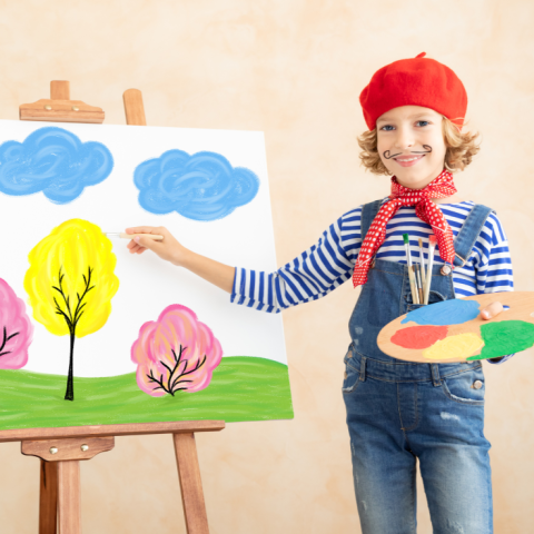 Young girl in beret holds a paint palette and brush in front of a canvas with art