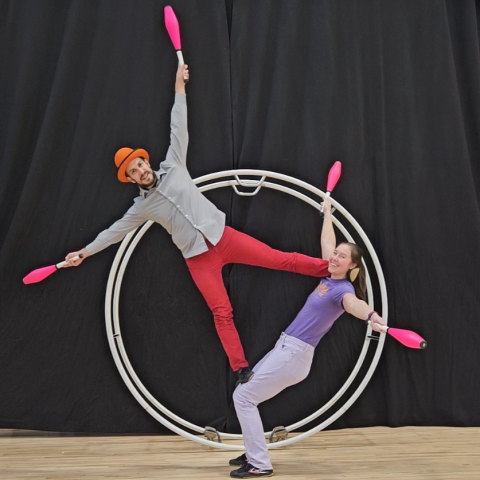 A man and woman with juggling pins balancing on a German wheel