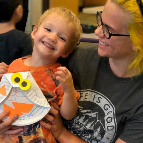 Smiling blonde boy sitting on his mother's lap while she looks down at him and smiles