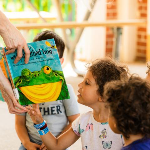 Children look at a colorful library book being held by an adult