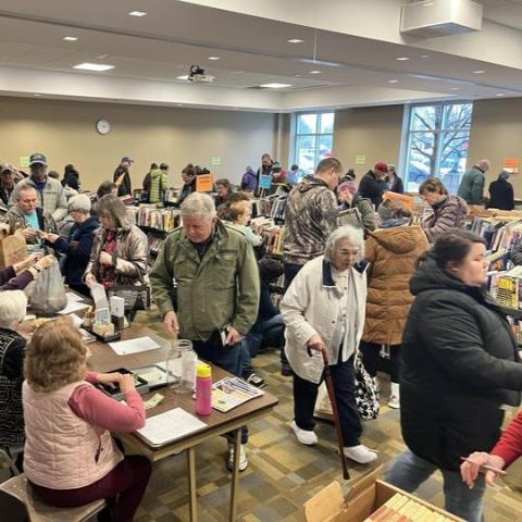 A crowded room of people browsing and buying books