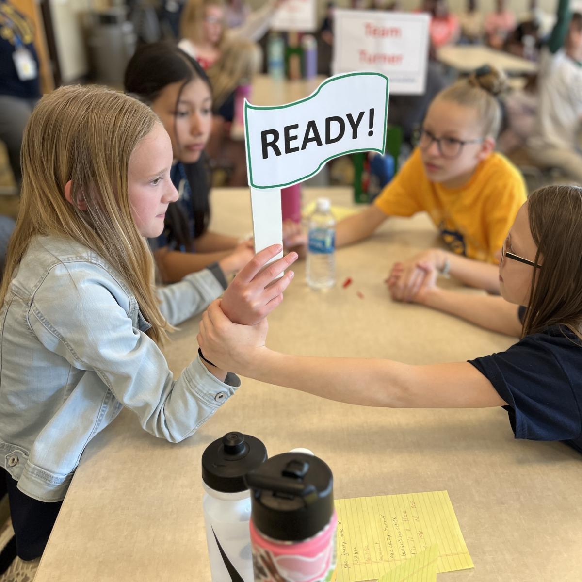 Four girls hold hands around the table while holding a sign that reads "ready"