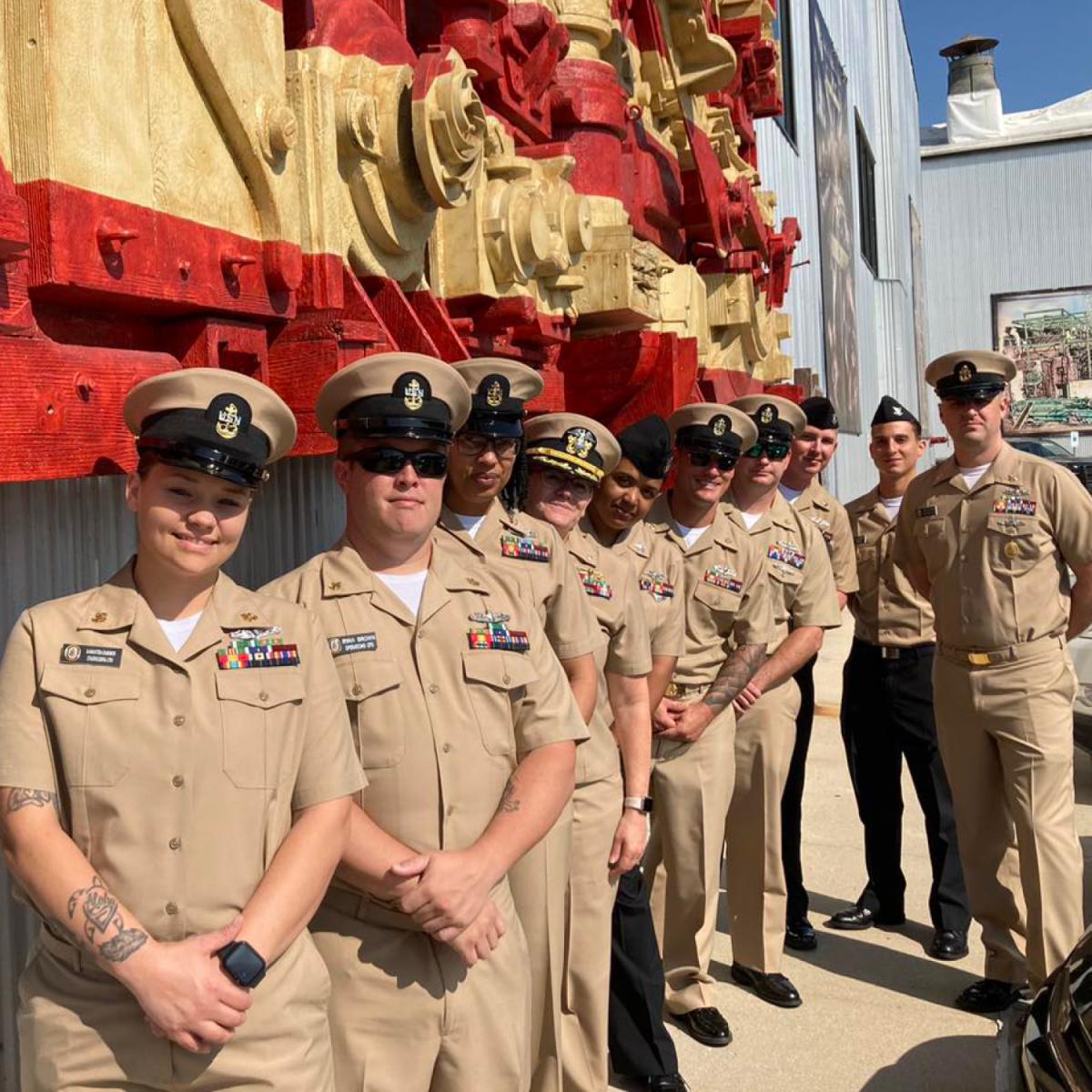 Naval officers stand in front of a patriotic work of art