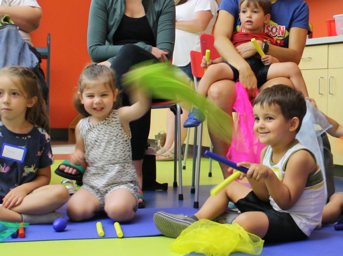 Children sitting on the floor waving colorful scarves as parents sit in chairs