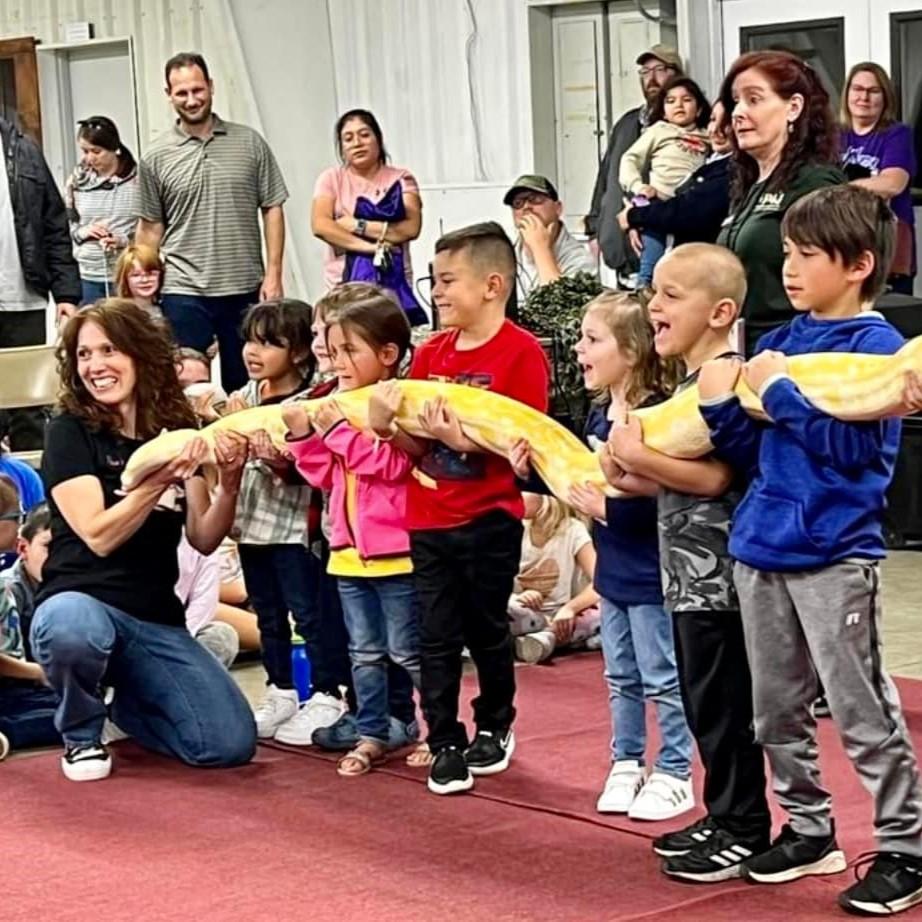 A presenter and several children hold a large snake