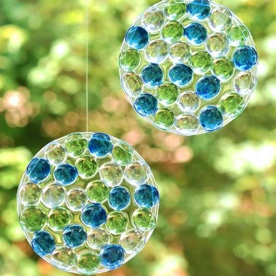 Two blue and green suncatchers hanging in front of greenery 