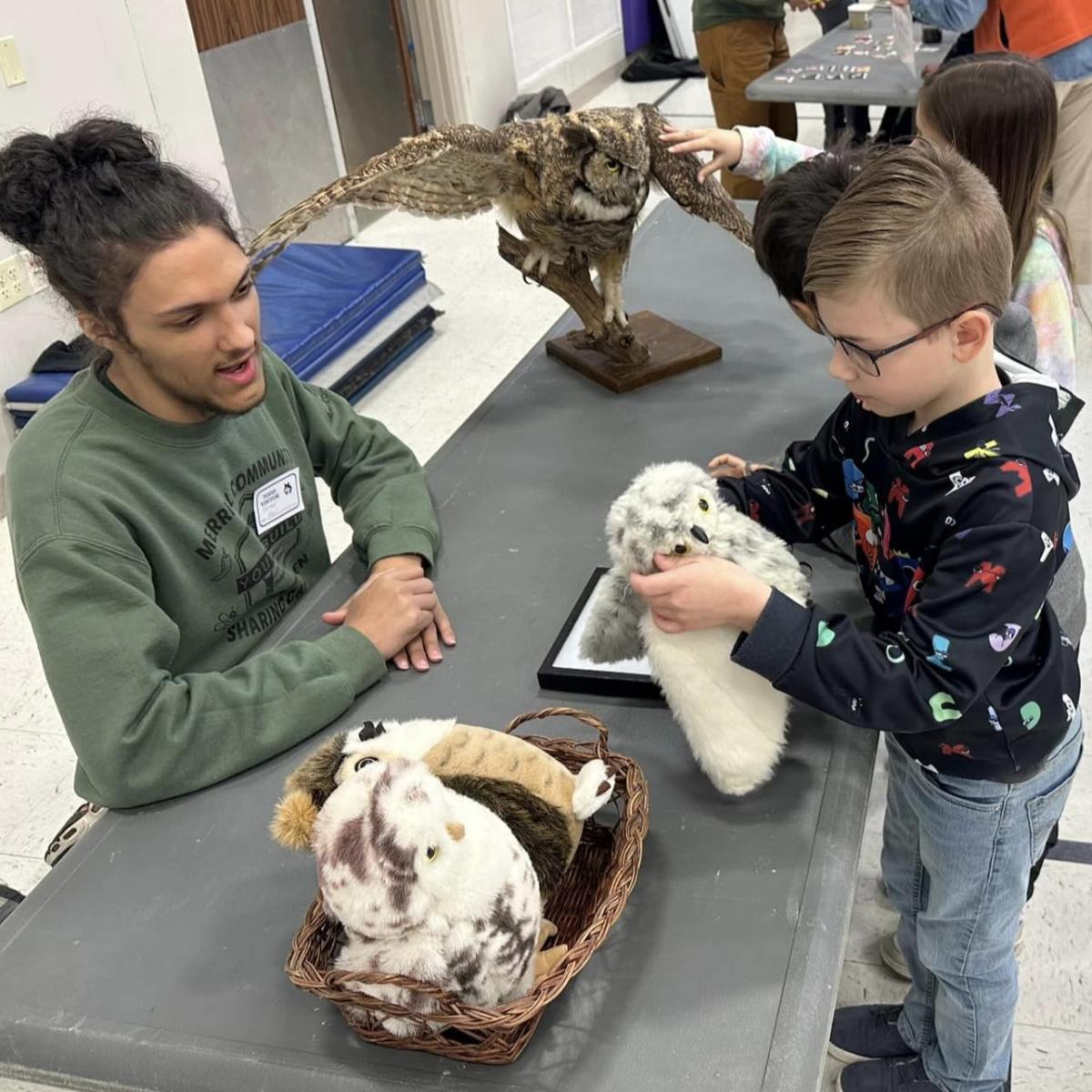 Young boy interacts with owl exhibit while an older teen talks