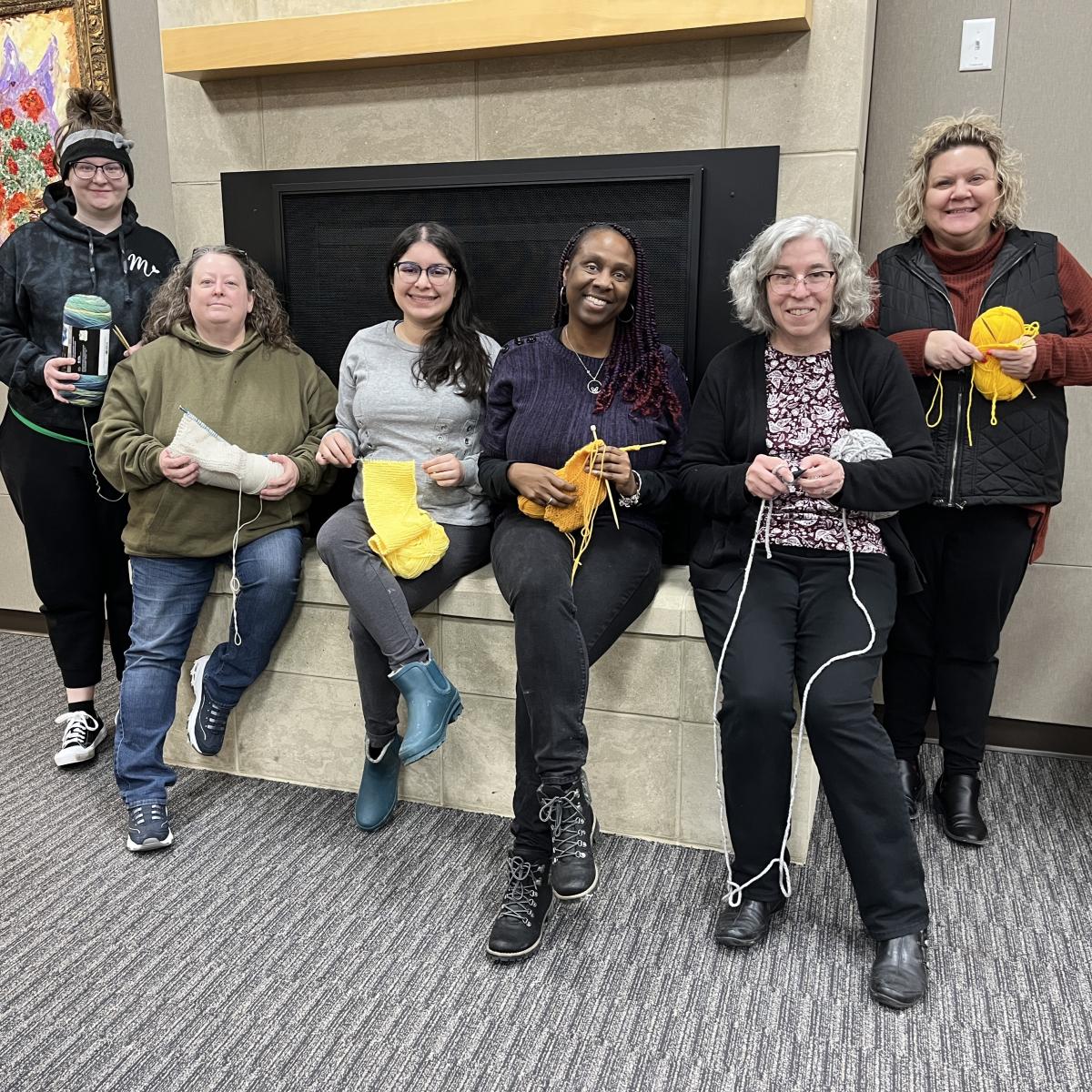 Women holding yarn projects standing in front of a fireplace