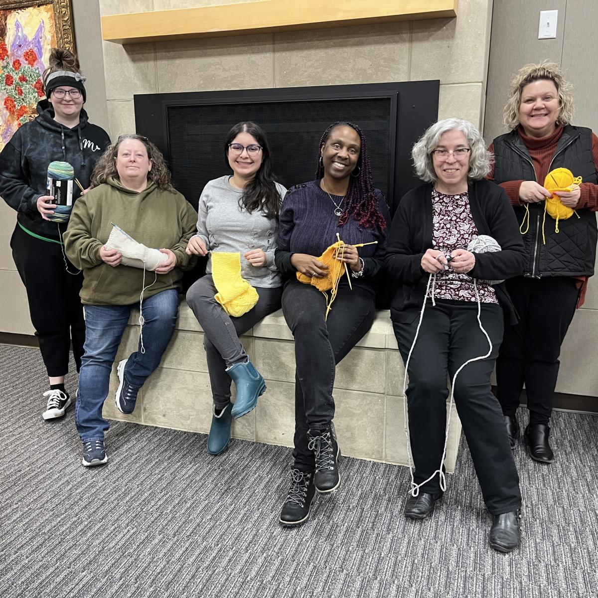 Women holding yarn projects standing in front of a fireplace