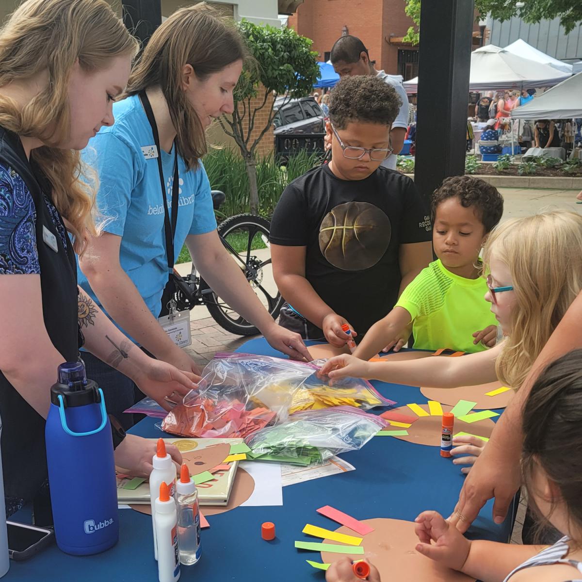 Adults leading kids in craft activity at table with blue tablecloth