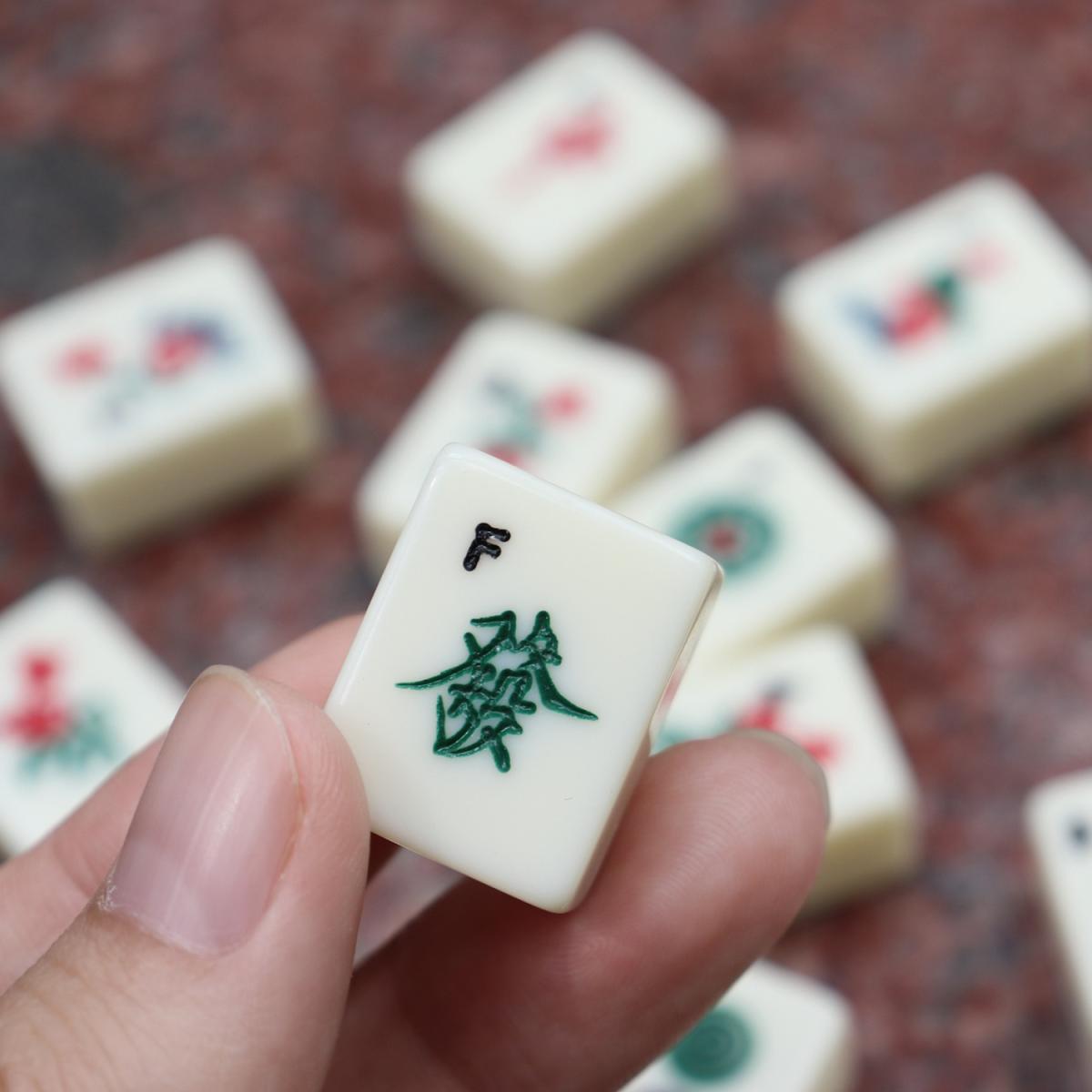 Hand holding a mahjong tile over a table of other tiles