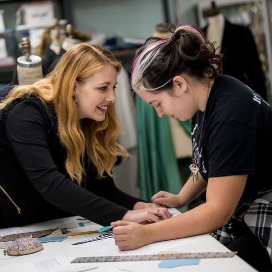 Two young women work together on a drafting table