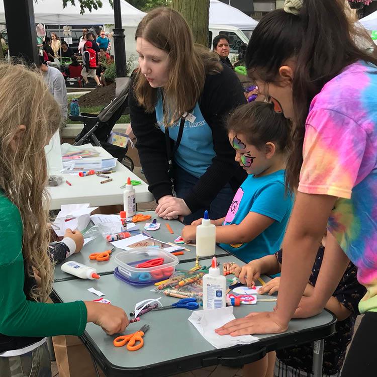 Library staff helping children with a craft at a table