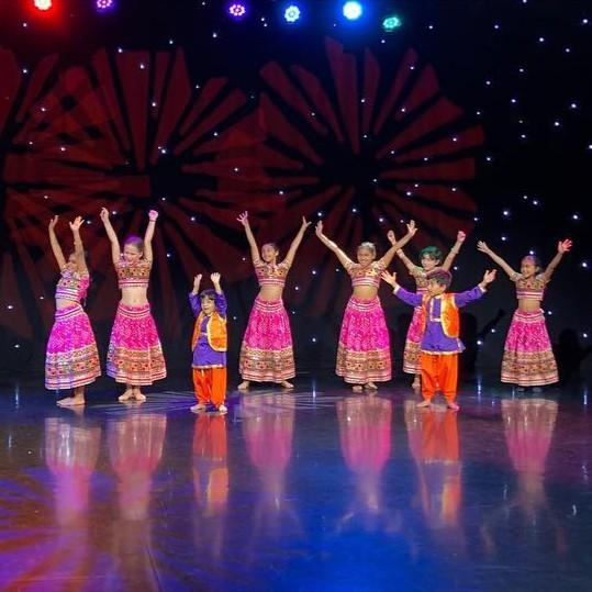 Children dressed in traditional Indian costumes dancing with their hands in the air