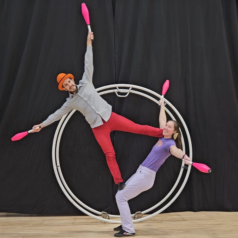 A man and woman with juggling pins balancing on a German wheel